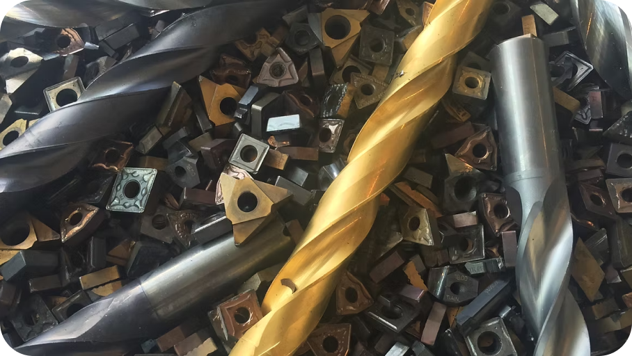 Brocas helicoidales y numerosas plaquitas de corte metalicas apiladas en distintos tonos dorado y gris sobre superficie industrial