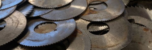 Discos metálicos circulares dentados apilados como chatarra industrial, con superficies desgastadas, rayadas y manchas de óxido en primer plano.