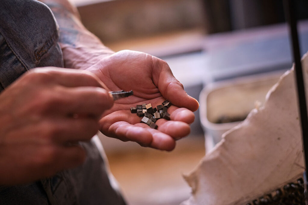 Primer plano de las manos de un trabajador sosteniendo pequenos fragmentos metalicos cuadrados y manipulandolos sobre superficie industrial
